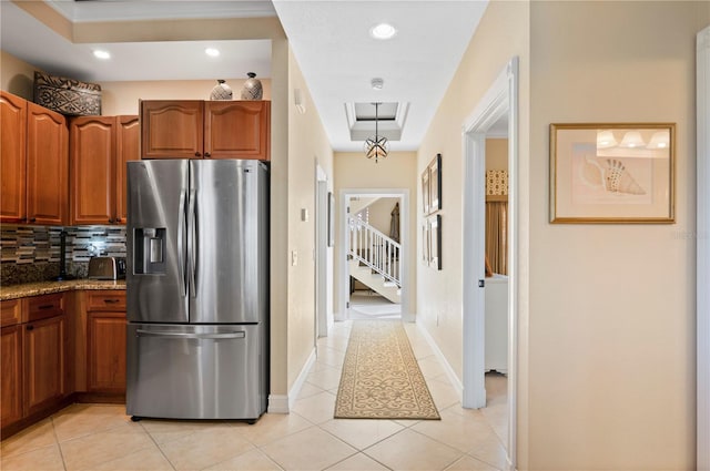 kitchen featuring light tile patterned flooring, stainless steel fridge with ice dispenser, a raised ceiling, dark stone counters, and backsplash