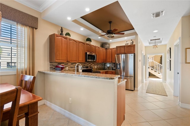 kitchen with appliances with stainless steel finishes, kitchen peninsula, tasteful backsplash, light stone counters, and a tray ceiling