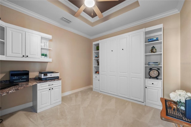 office with ceiling fan, a tray ceiling, built in desk, ornamental molding, and light carpet