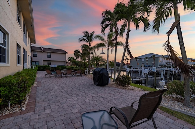 patio terrace at dusk featuring a water view and grilling area