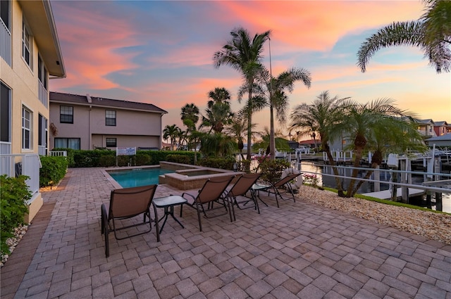 pool at dusk featuring a water view, a jacuzzi, and a patio