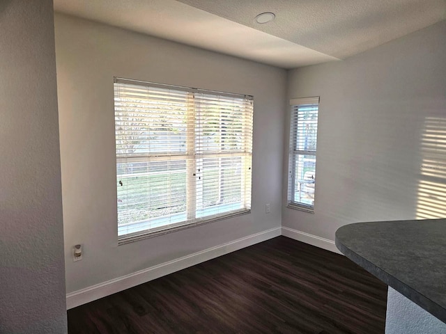 unfurnished dining area featuring dark wood-type flooring and a textured ceiling