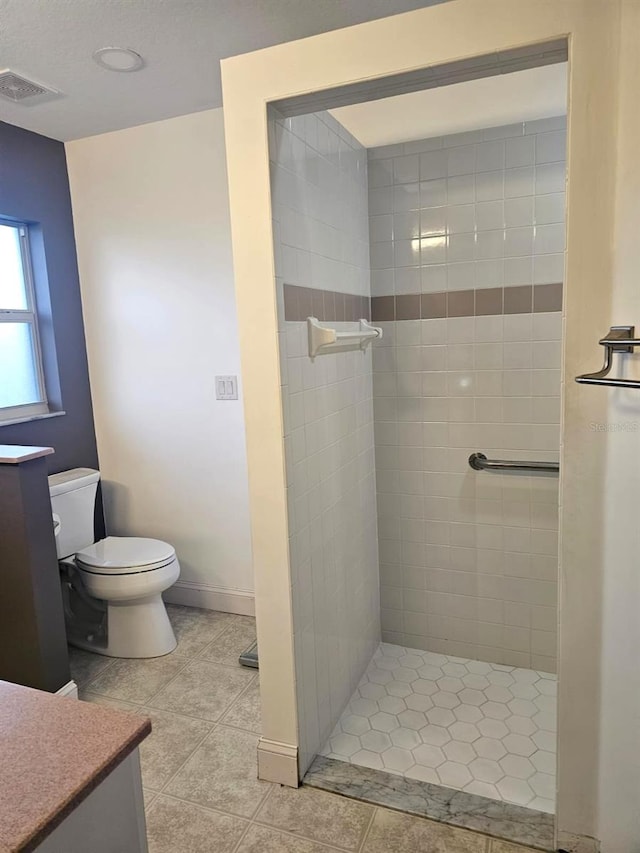 bathroom featuring vanity, tile patterned floors, toilet, and a tile shower