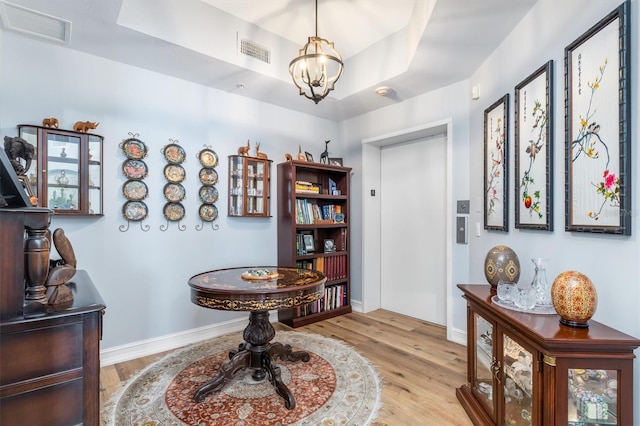 interior space featuring a raised ceiling, a notable chandelier, and light hardwood / wood-style floors