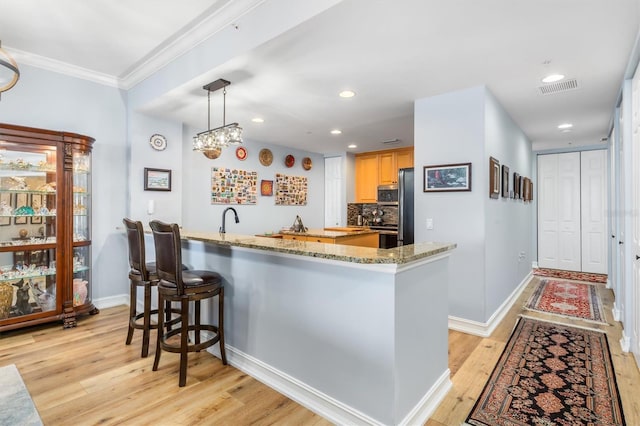 kitchen featuring pendant lighting, light hardwood / wood-style flooring, appliances with stainless steel finishes, tasteful backsplash, and light stone countertops