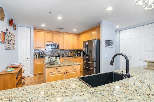 kitchen featuring light stone counters, stainless steel appliances, light brown cabinetry, and sink