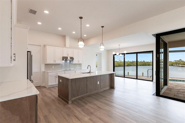 kitchen with pendant lighting, sink, white cabinets, light stone counters, and a water view