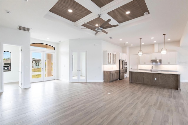 unfurnished living room featuring french doors, coffered ceiling, sink, light hardwood / wood-style flooring, and a high ceiling