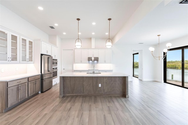 kitchen featuring pendant lighting, white cabinetry, high end fridge, a center island with sink, and light wood-type flooring