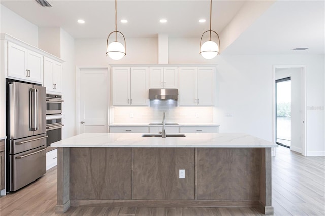 kitchen with stainless steel appliances, a center island with sink, white cabinets, and decorative light fixtures