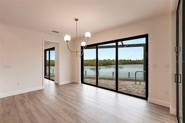 unfurnished dining area featuring a water view, a chandelier, and light hardwood / wood-style flooring