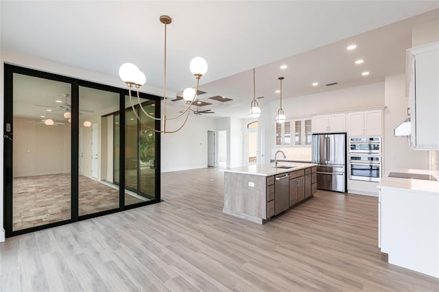 kitchen featuring sink, hanging light fixtures, stainless steel appliances, white cabinets, and a center island with sink