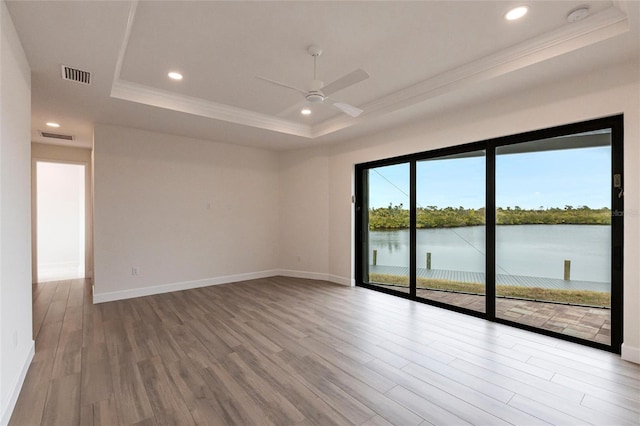 empty room featuring hardwood / wood-style floors, ornamental molding, ceiling fan, a raised ceiling, and a water view