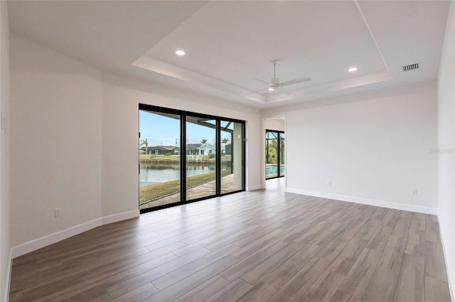 unfurnished room with light wood-type flooring, a raised ceiling, ceiling fan, and a water view