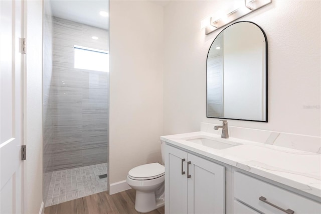 bathroom featuring vanity, hardwood / wood-style flooring, toilet, and a tile shower