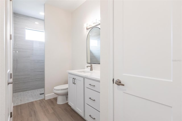 bathroom featuring vanity, wood-type flooring, toilet, and a tile shower