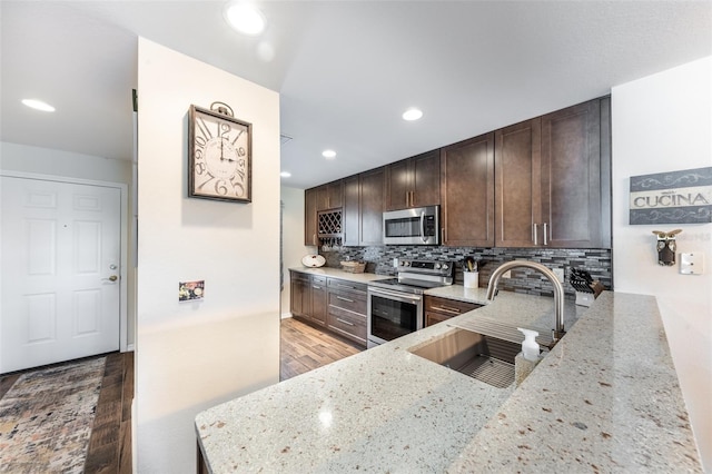 kitchen with light stone counters, stainless steel appliances, sink, and tasteful backsplash