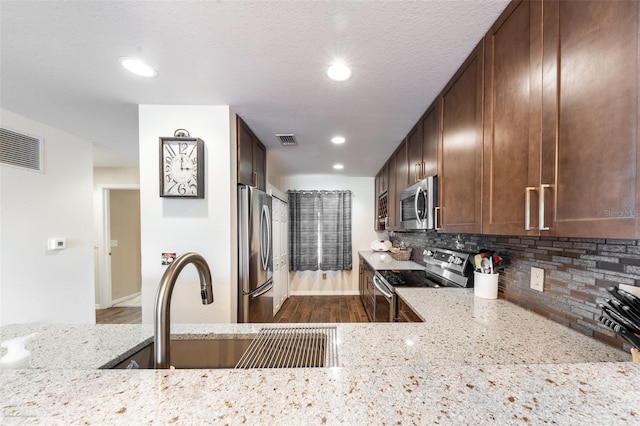 kitchen featuring sink, light stone counters, a textured ceiling, stainless steel appliances, and backsplash