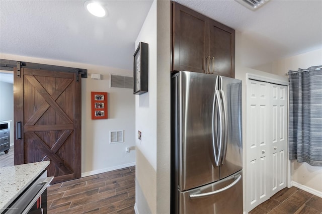 kitchen featuring light stone counters, dark brown cabinetry, stainless steel refrigerator, and a barn door