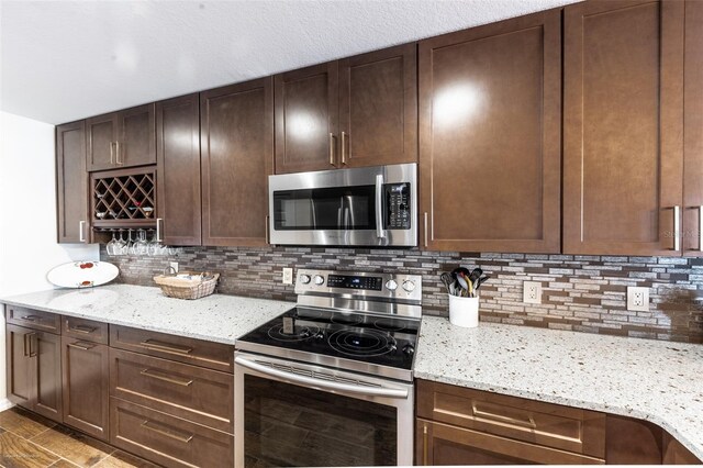 kitchen featuring dark brown cabinetry, light stone countertops, backsplash, and stainless steel appliances