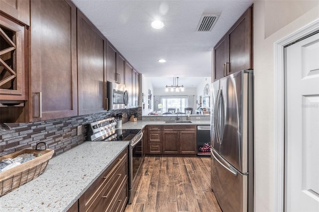 kitchen with sink, dark wood-type flooring, stainless steel appliances, tasteful backsplash, and light stone countertops