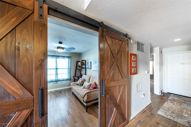 corridor featuring a barn door, dark wood-type flooring, and a textured ceiling