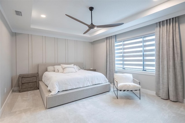 bedroom with light colored carpet, a raised ceiling, and ceiling fan