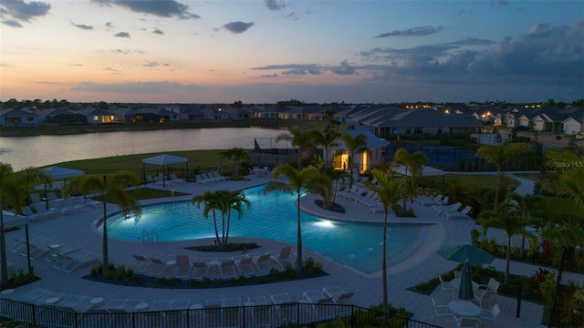 pool at dusk with a residential view, a community pool, a patio area, a water view, and fence