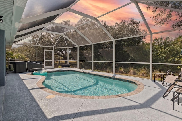 pool at dusk featuring a lanai, a patio area, and a hot tub