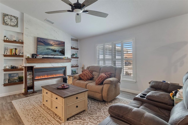 living room featuring vaulted ceiling, a large fireplace, built in shelves, and light hardwood / wood-style floors