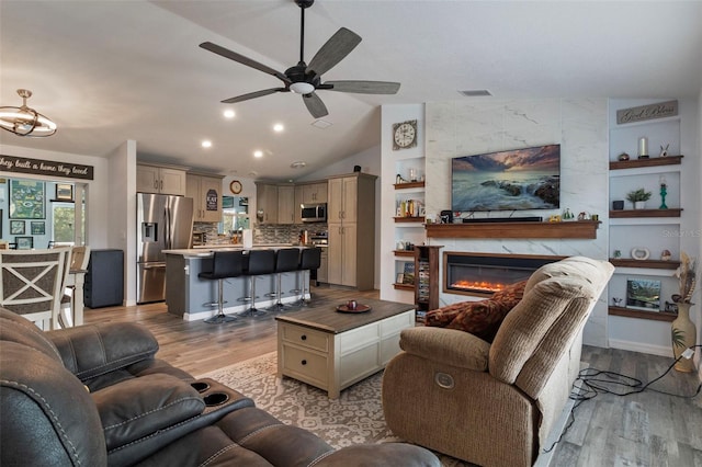 living room featuring built in shelves, vaulted ceiling, light wood-type flooring, ceiling fan, and a high end fireplace