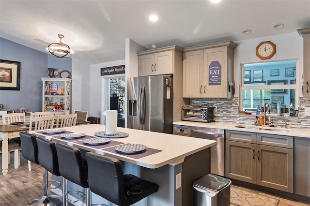 kitchen featuring sink, light hardwood / wood-style flooring, appliances with stainless steel finishes, backsplash, and a kitchen bar