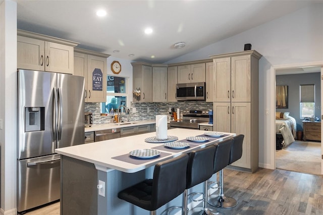 kitchen with sink, vaulted ceiling, a kitchen breakfast bar, a kitchen island, and stainless steel appliances