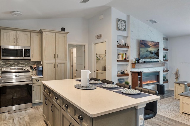 kitchen featuring lofted ceiling, appliances with stainless steel finishes, a kitchen island, and light hardwood / wood-style flooring