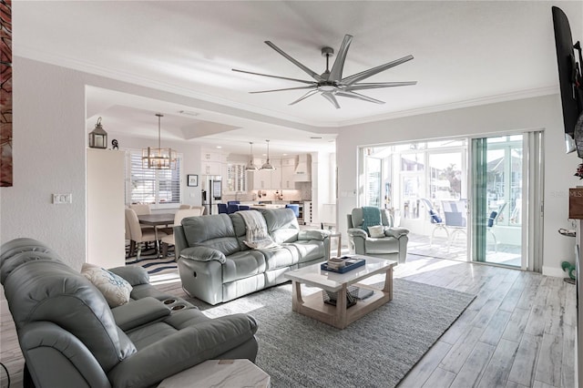 living room with ceiling fan with notable chandelier, light hardwood / wood-style flooring, and ornamental molding