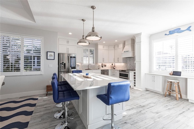 kitchen with premium range hood, white cabinetry, decorative light fixtures, appliances with stainless steel finishes, and a kitchen island