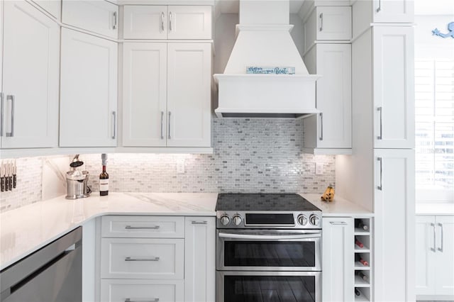 kitchen with premium range hood, appliances with stainless steel finishes, white cabinets, backsplash, and light stone counters