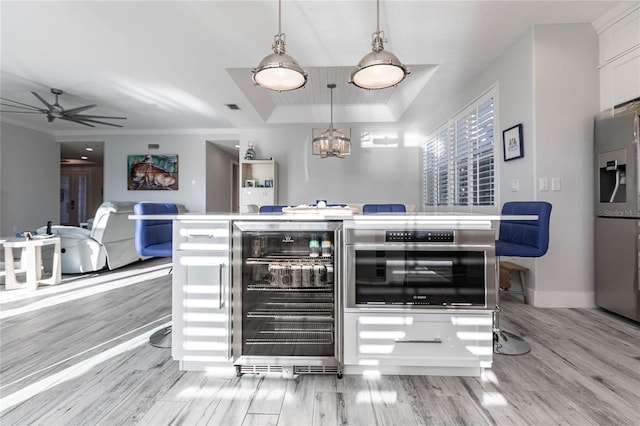 kitchen with pendant lighting, white cabinets, wine cooler, a tray ceiling, and stainless steel appliances