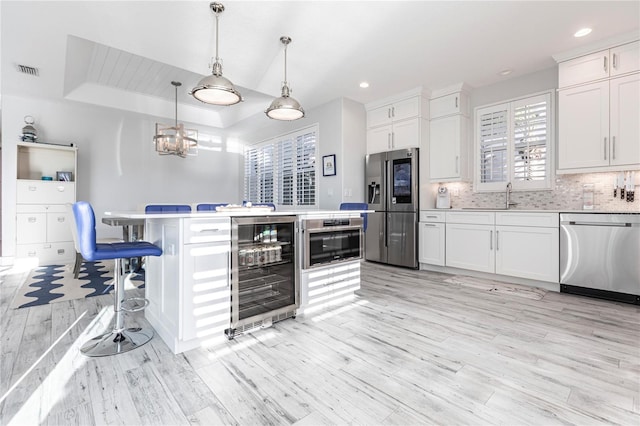 kitchen with pendant lighting, appliances with stainless steel finishes, white cabinetry, a center island, and wine cooler