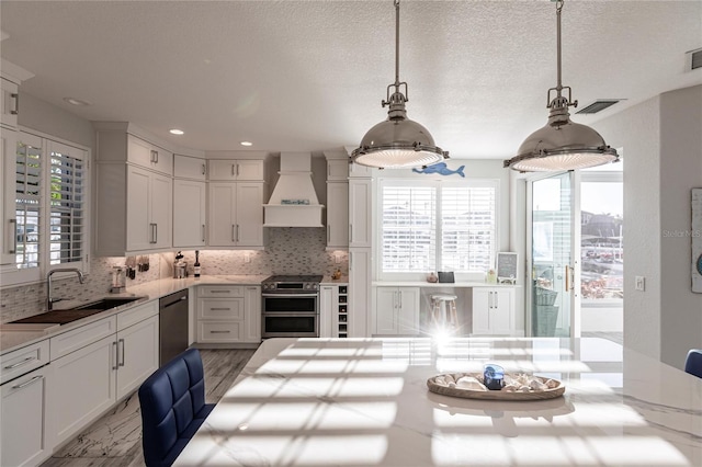 kitchen with premium range hood, stainless steel stove, black dishwasher, white cabinets, and hanging light fixtures