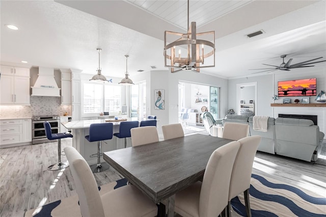 dining area featuring lofted ceiling, ornamental molding, ceiling fan with notable chandelier, and light hardwood / wood-style flooring