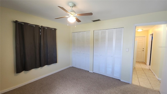 unfurnished bedroom with light carpet, two closets, and ceiling fan