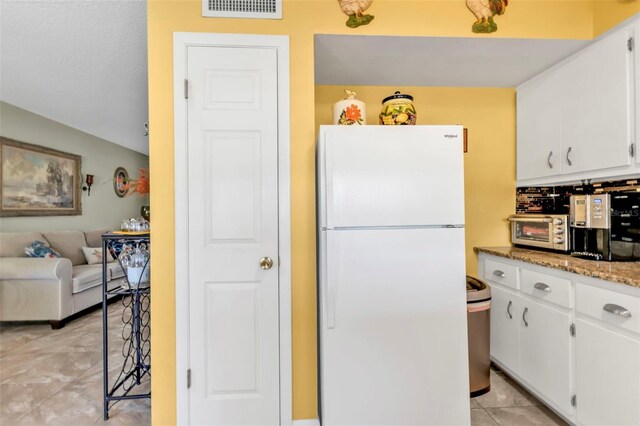 kitchen featuring light tile patterned floors, light stone countertops, white cabinets, and white fridge