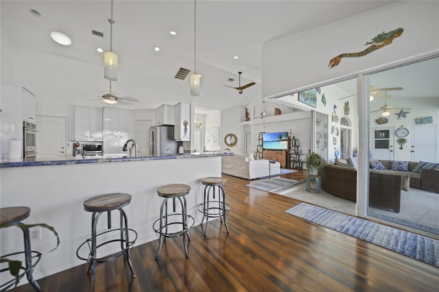 kitchen with white cabinetry, stainless steel fridge, dark stone counters, hanging light fixtures, and kitchen peninsula