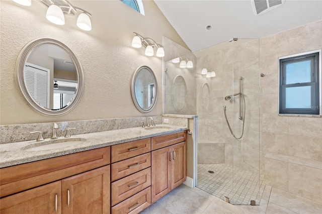 bathroom with tile patterned flooring, vanity, lofted ceiling, and a tile shower