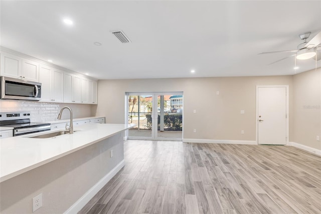 kitchen with sink, light hardwood / wood-style flooring, appliances with stainless steel finishes, white cabinets, and decorative backsplash