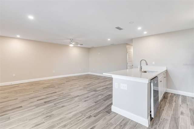 kitchen with sink, dishwasher, ceiling fan, light hardwood / wood-style floors, and an island with sink