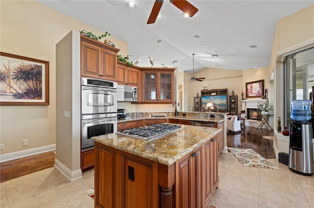 kitchen featuring ceiling fan, stainless steel appliances, light stone counters, a kitchen island, and kitchen peninsula