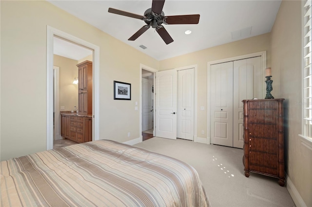 bedroom with ceiling fan, connected bathroom, light carpet, and two closets