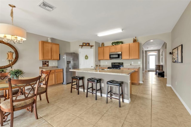 kitchen featuring an island with sink, a kitchen breakfast bar, hanging light fixtures, light tile patterned floors, and stainless steel appliances